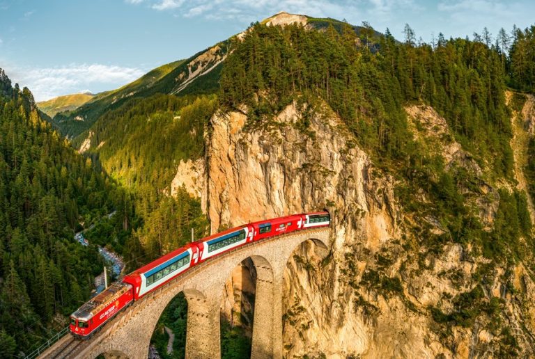 İsviçre Alplerinde tarihi taş viyadükten geçen panoramik kırmızı tren, Swiss Travel Pass ile keşfedilebilecek eşsiz manzaraları gösteriyor.